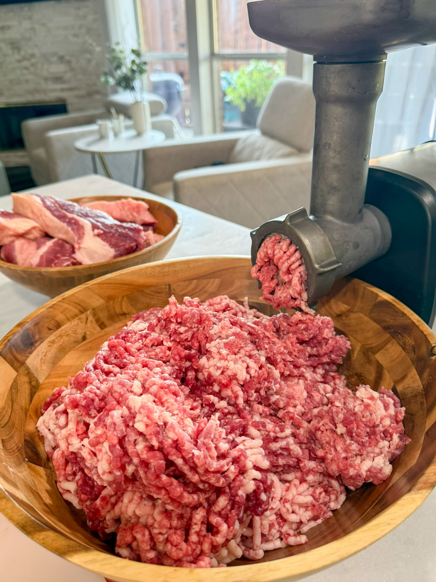 A meat grinder, actively grinding meat into a wooden bowl.