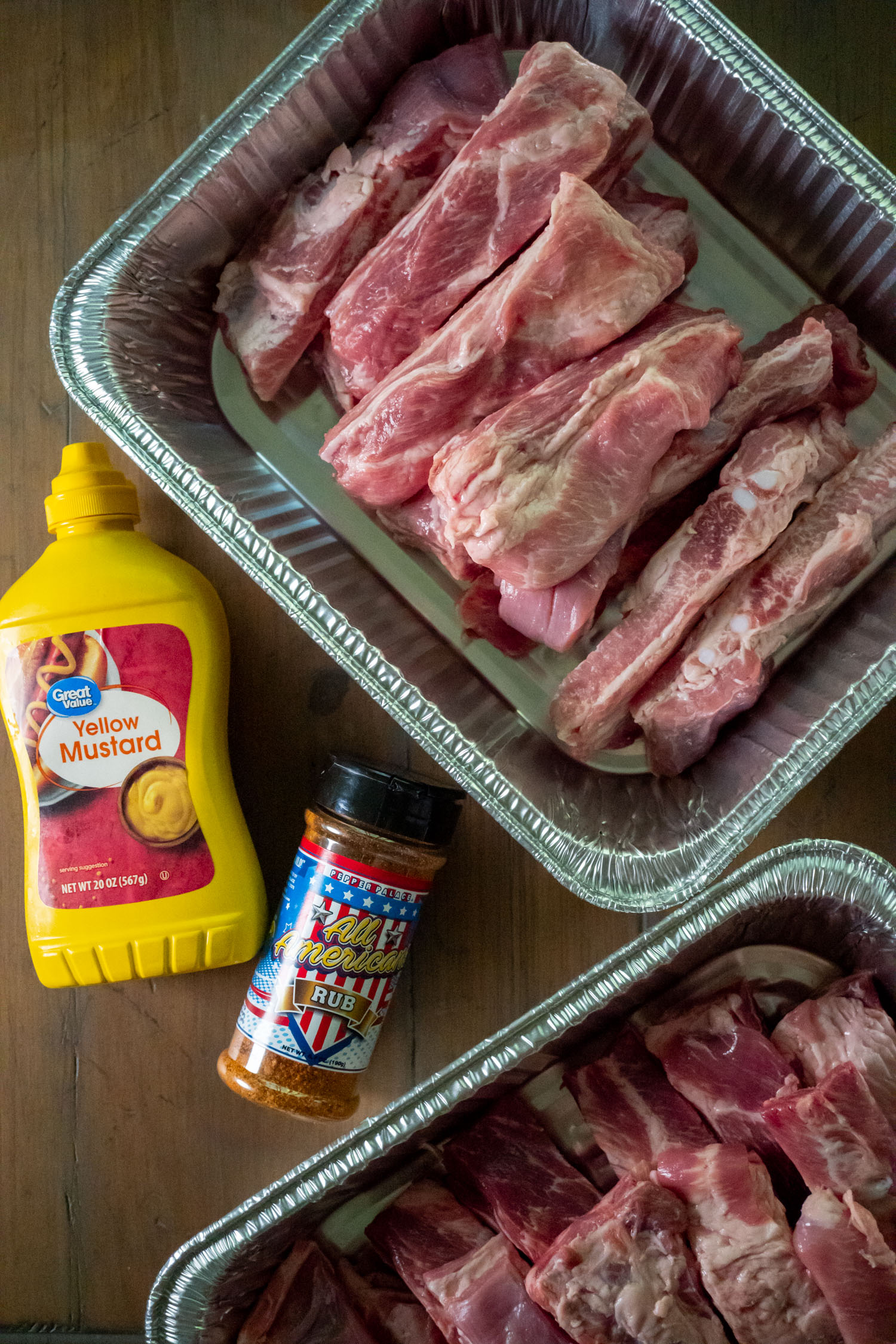 raw pork ribs in pans next to mustard and pork rub.